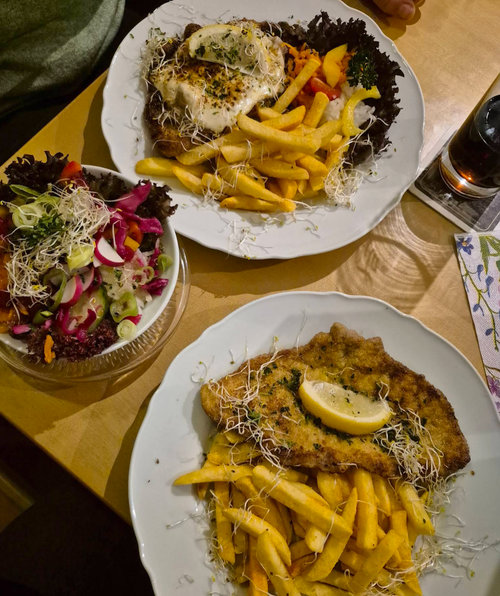 Zwei Teller mit gebratenem Fleisch, Pommes und gemischtem Salat, dekoriert mit Zitrone.